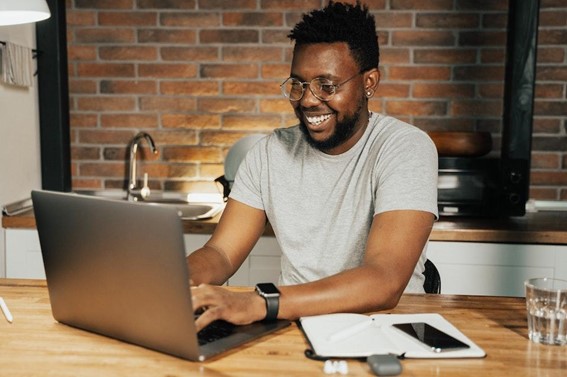 Ferramentas: Rapaz negro e feliz, navegando na internet pela tela de um notebook